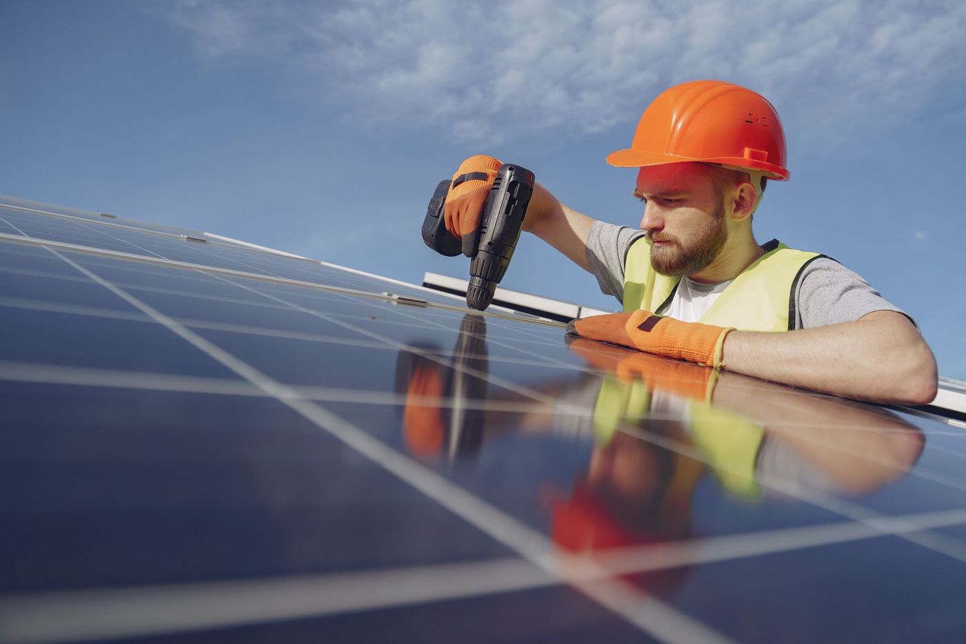 Solar installer fastening a rooftop solar panel with a drill